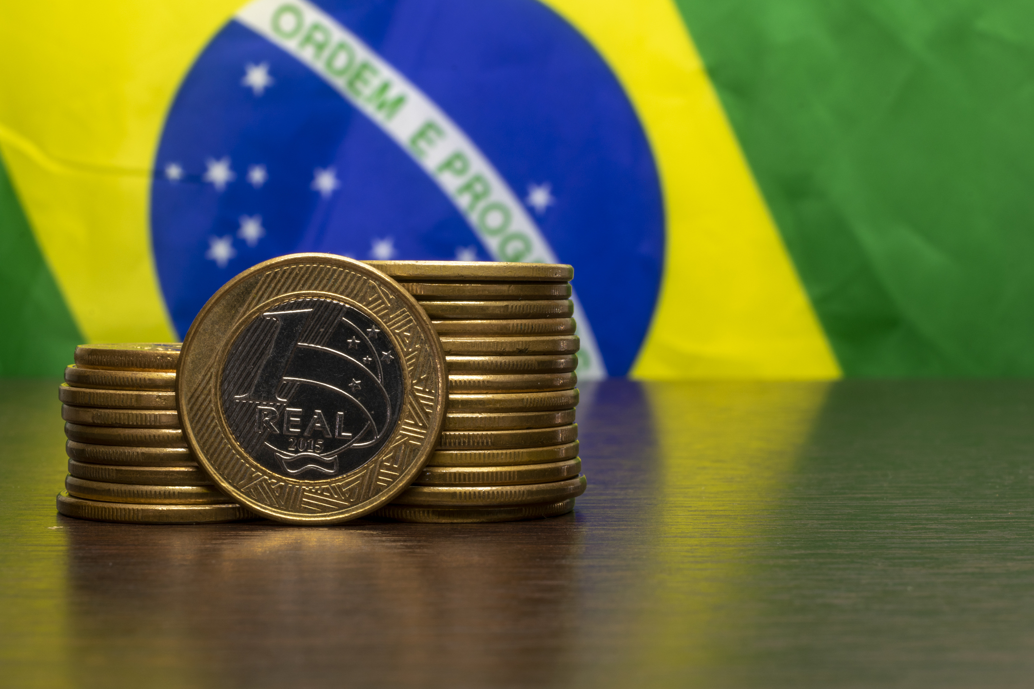 stack of Brazilian coins with a real highlighted and the Brazilian flag in the background. selective focus.